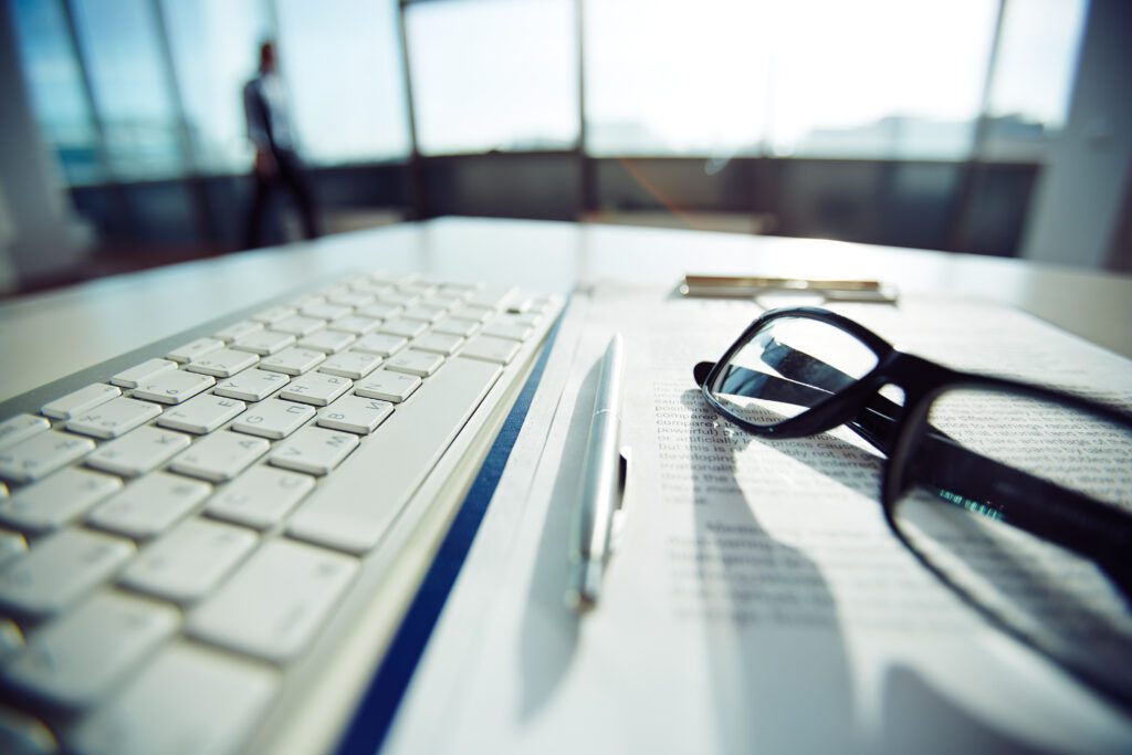 White keyboard with pen and glasses on documents