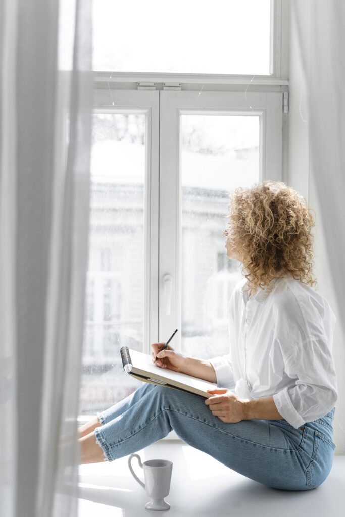 Woman writing in a notebook by the window