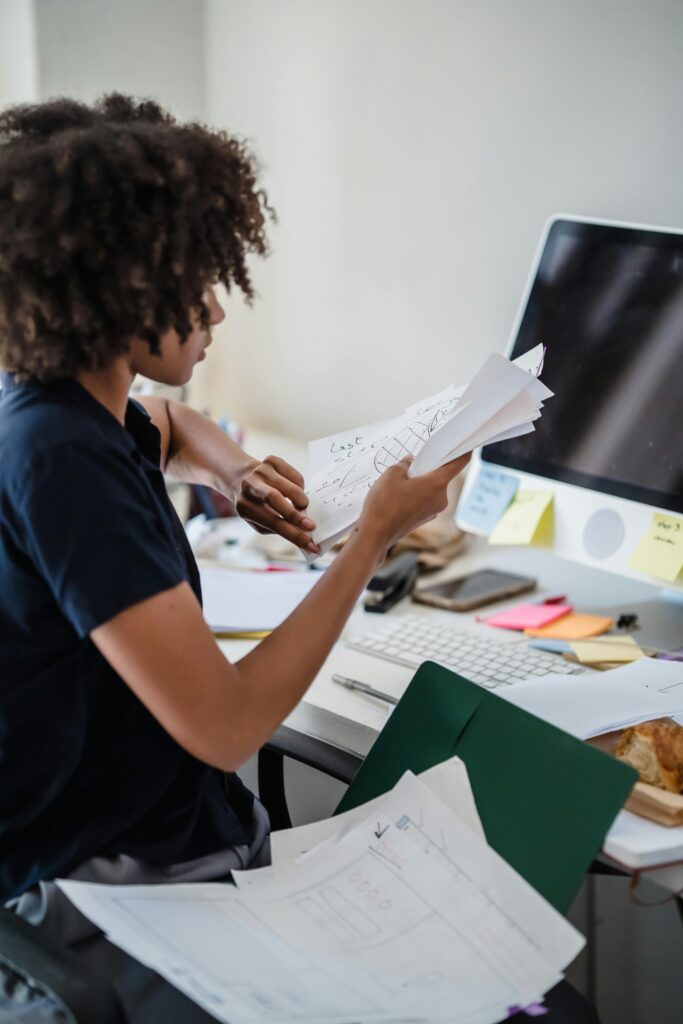 Person sorting papers at desk with computer